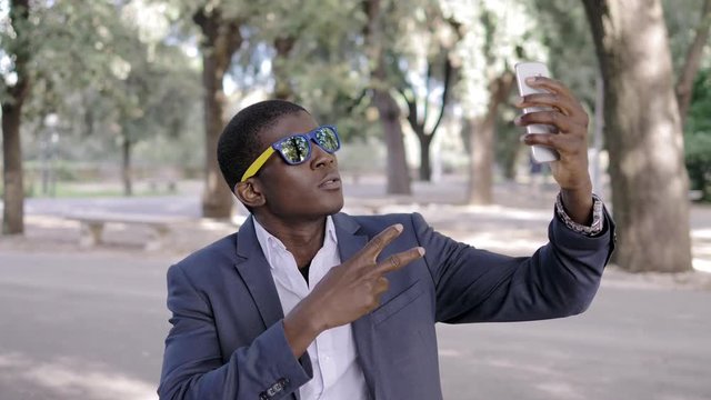 confident black businessman wearing sunglasses taking selfie in the park