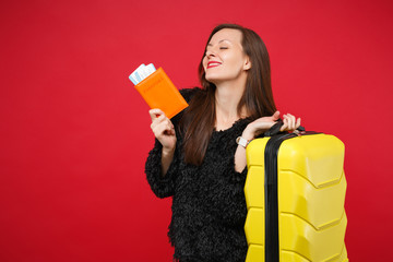 Happy young woman in black fur sweater with closed eyes hold suitcase, passport, boarding pass ticket isolated on bright red background. People sincere emotions, lifestyle concept. Mock up copy space.