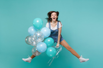 Cheerful young woman in denim clothes keeping mouth open, jumping high, celebrating, hold colorful...