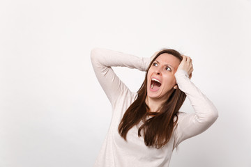 Portrait of screaming irritated young woman in light clothes clinging to head, looking aside isolated on white wall background in studio. People sincere emotions lifestyle concept. Mock up copy space.