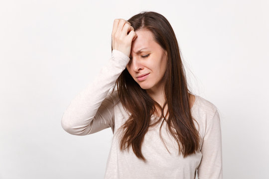 Tired crying disconcerted young woman in light clothes keeping eyes closed, putting hands on head isolated on white background in studio. People sincere emotions lifestyle concept. Mock up copy space.