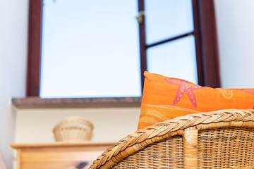 One comfortable vintage straw armchair home or house living room or bedroom by open window and sky with beach orange pillow closeup