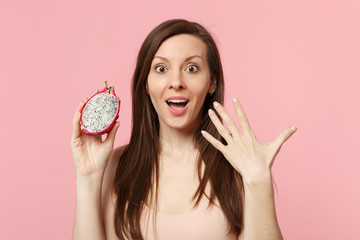 Excited young girl in light clothes holding in hand half of fresh ripe pitahaya dragon fruit...