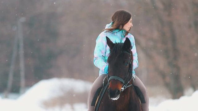 An smiling young woman on a horseback in a winter forest