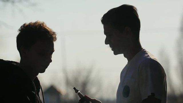 Silhouette of young man that throwing out cigarette from hand of his smoking friend and gives him to e-cigarette try vaping