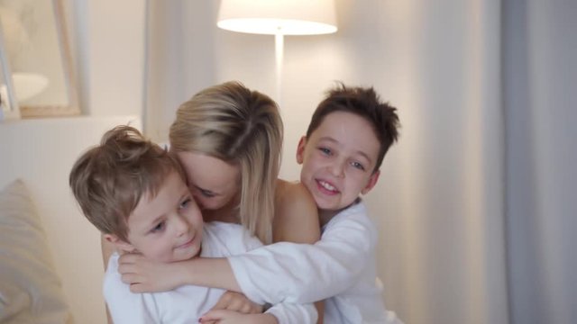 Happy family - mother with two sons hugging in bed