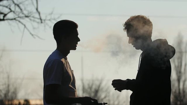 Silhouette of young man that stopped his friend that took out a pack of cigarettes and gives him his vaporizer to try vaping