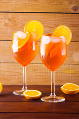 Cocktail aperol spritz on wooden boards. Two glasses with summer alcoholic cocktail with orange slices. Italian cocktail aperol spritz on wooden background. Trend drink