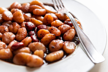 Closeup macro of fresh red wine sauce potato gluten free wheat gnocchi on white plate in Italian Italy restaurant with fork and olive oil