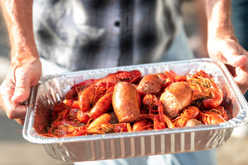 Closeup of lobsters and seafood with hands holding tray of red shellfish in New Orleans street food