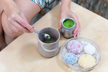 Green matcha teacup and mochi rice cake Japanese dessert wagashi colorful daifuku with woman girl hand preparing tea powder measuring spoon on table