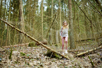 Naklejka na ściany i meble Cute young girl having fun during forest hike on beautiful early spring day. Active family leisure with kids.