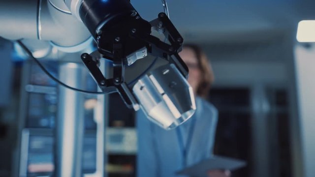Close Up of a Futuristic Robotic Arm Moving a Metal Detail. Team of Engineers Observe This Technologically Advanced Process. They are in a High Tech Research Laboratory with Modern Equipment.