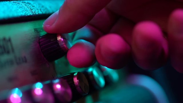 View of the control panel on a guitar amplifier. Tumblers, knobs and buttons. Male hand turn on and increasing music volume on amp. Colorful neon light