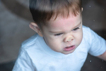 Cute baby boy looking in the window glass with reflection. Loneliness of children. Orphanage and orphans