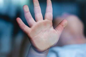 Child's small hand is pressed against the window glass with reflection. Loneliness of children....