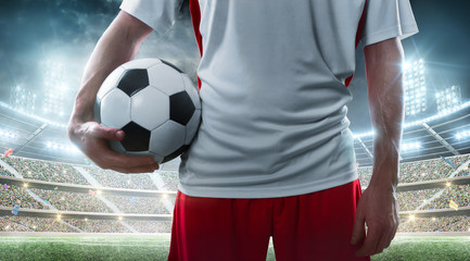 Sport. Professional soccer player holding soccer ball on the stadium background. Close up