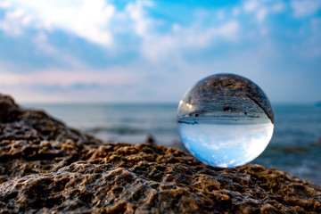 Crystal glass balls are displayed on a rocky coast with turquoise clouds covered with a summer background.
