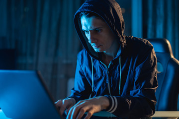 Cybercriminal hacker in the hood typing program code while stealing access databases with...