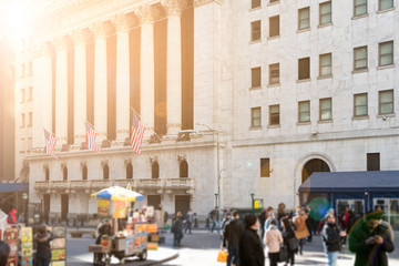 Sunlight shines on the crowds of people and historic buildings along Wall Street in the financial...