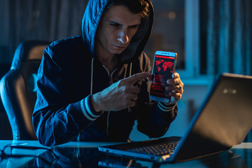 Hacker in the hood holding the phone in his hands trying to steal access databases with passwords....