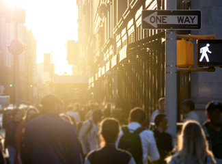 Crowd of anonymous people walking down the sidewalk with bright sunlight in the background on a...