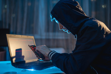 Male hacker in the hood holding the phone in his hands trying to steal access databases with...