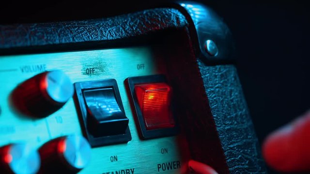 Power switch tumbler being turned on and off by musician. Colorful neon light. Close up view. Concert, music concept