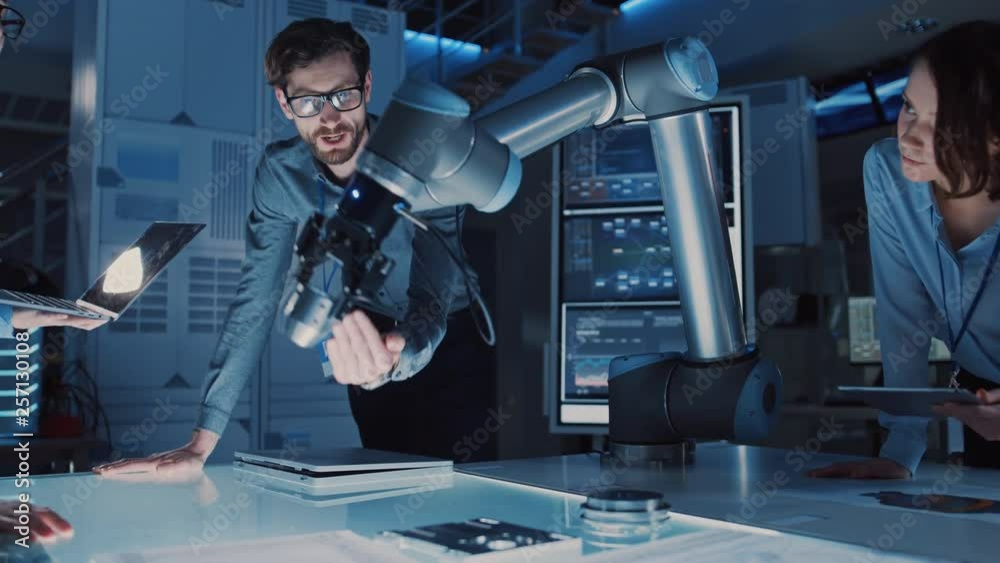 Leinwandbilder Diverse Team of Engineers with Laptop and a Tablet Analyse and Discuss How a Futuristic Robotic Arm Works and Moves a Metal Object. They are in a High Tech Research Laboratory with Modern Equipment.