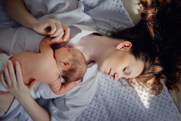 Obraz na płótnie Canvas A newborn baby boy is lying on mom's chest. In a bright room. In the sun