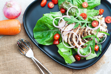 Top view. Grilled chicken salad with tomatoes and onions on black plate