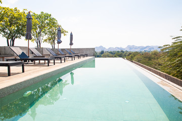 Kanchanaburi, Thailand - February 20, 2019 : Modern and simply design chaise lounge and swimming pool on the hotel roof top with mountain view