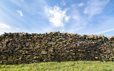Stone wall next to a grassy agricultural field on a sunny day in the Peak District, England.