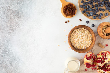 Top view and flat lay of oatmeal porridge in wooden ware with milk, red currant, blueberries, almonds, and garnet on textured concrete light table. Mock-up of food for healthy breakfast, flatlay