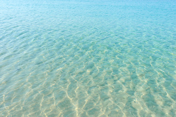 Clear blue water ripple on sandy beach. Sea water reflections surface. Tropical sunny summer day.