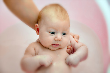 Mom bathes the newborn baby in a pink bathtub, close-up