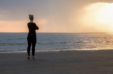 Fototapeta premium girl is waiting, standing on tiptoe, looking into the distance, barefoot on the sand, sunset on the bay