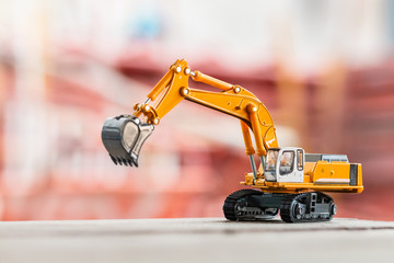 Yellow excavator model toy parked on floor ground on a construction site background.