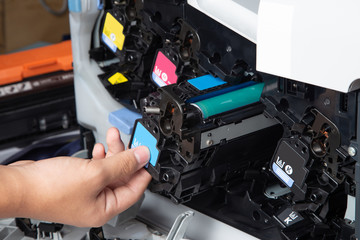 Business man or technician is checking and changing the printer equipment cartridges tone of laser jet multi function printer in the office. Close-up shot of CMYK ink cartridges for laser printer. - obrazy, fototapety, plakaty