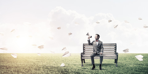 Businessman in summer park announcing something in loudspeaker and paper planes fly around