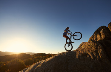 Silhouette of courageous cyclist balancing on back wheel on trial bicycle. Professional sportsman...