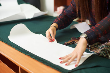 Tailor, designer workplace in atelier. Female hands making white chalk markings of paper patterns...