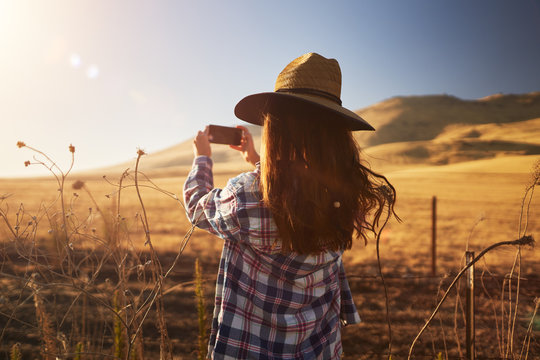 skinny girl wearing hat taking photo of rural california landscape