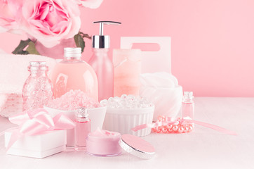 Elegant pink skin and body care products - cream, rose oil, liquid soap, salt, cotton towel and box - cosmetic accessories, romantic flowers on white wood table.