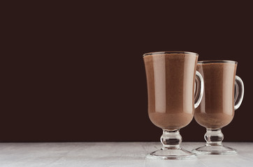 Elegant hot chocolate in irish coffee glass on dark brown background, copy space.