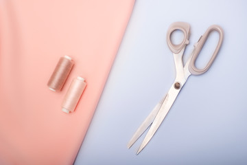 Sewing tools: pink fabric, scissors, colored spools of thread on a blue background (top view, flat lay)