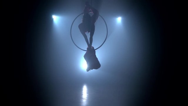 Gymnasts performs a trick in the aerial hoop. Black smoke background. Silhouette