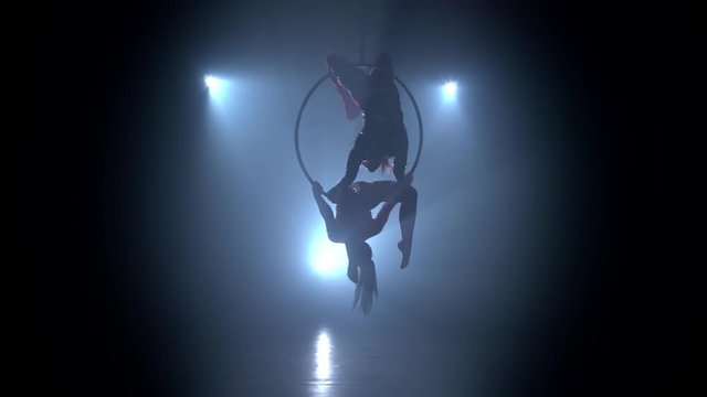 Two girls spinning on a hoop on stage. Black smoke background. Silhouette