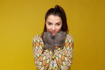 Close up portrait of cute pleased young attractive female, keeping head on arms, wearing cozy colorful knitted outfit, going to say good buy for winter, ready for spring and love. Happiness concept.