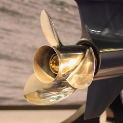 Close up golden stainless steel motor boat propeller on gear drive shaft of outboard motor - rear side view in blue color